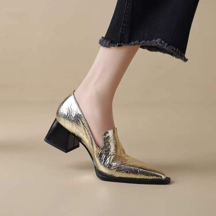 Shiny gold pointed-toe block heel shoe worn with frayed black jeans on beige background
