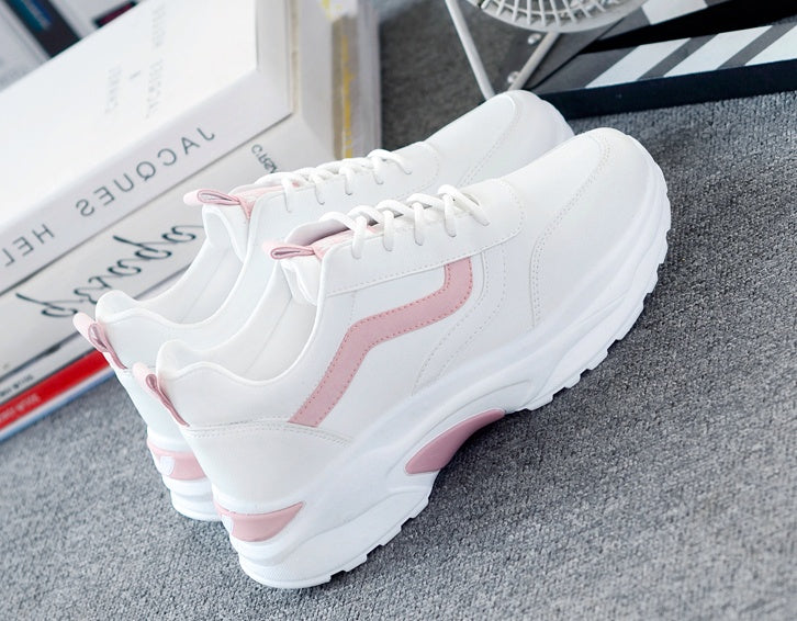 White chunky sneakers with pink accents on grey carpet near stacked books and decor