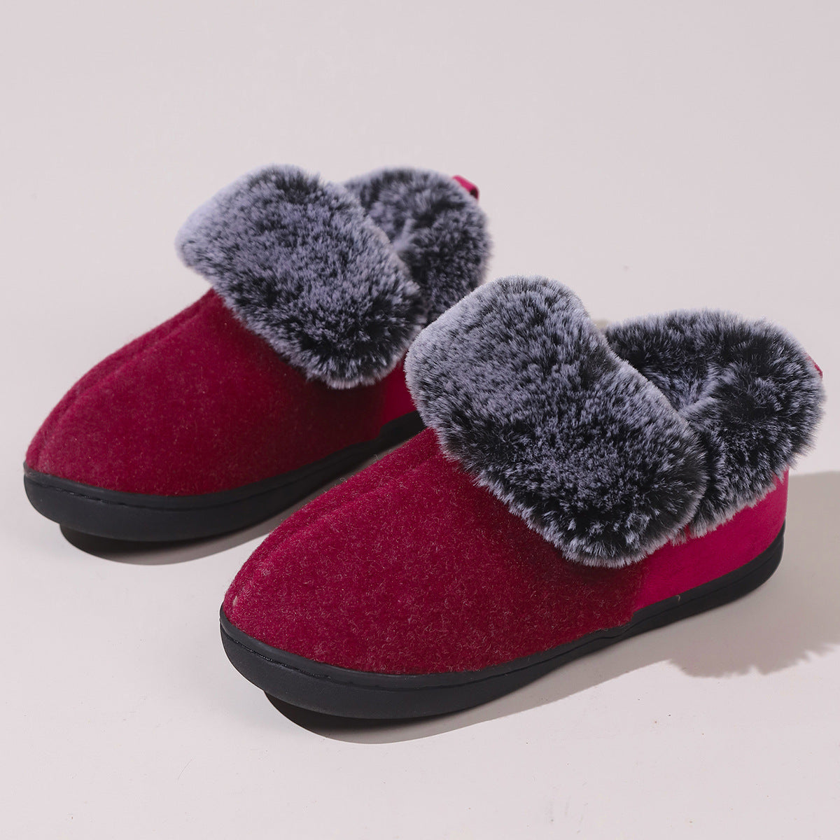 Pair of red indoor slippers with thick gray faux fur lining and black soles on white background