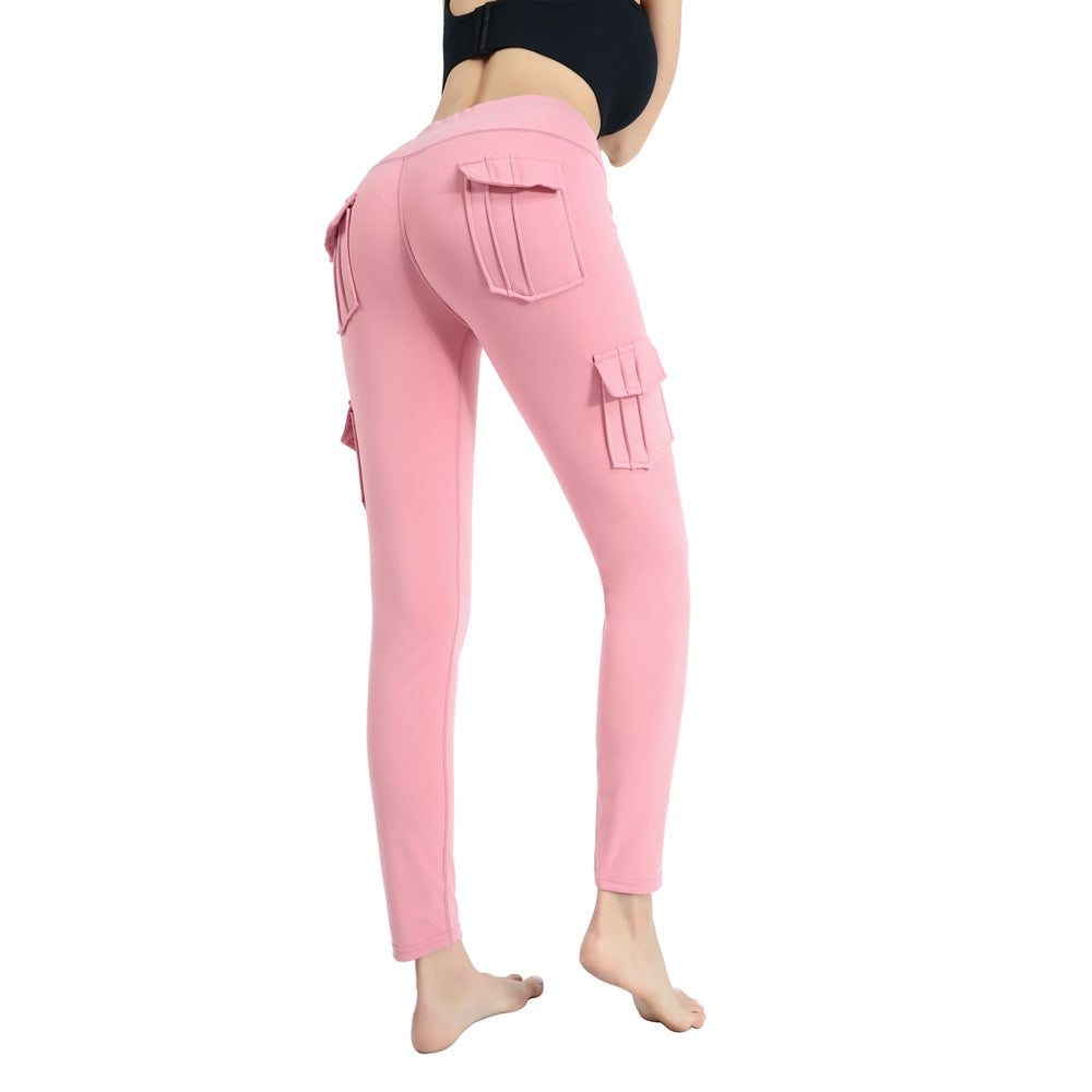 Woman wearing pink cargo leggings with multiple pocket flaps and a black crop top, barefoot on white background