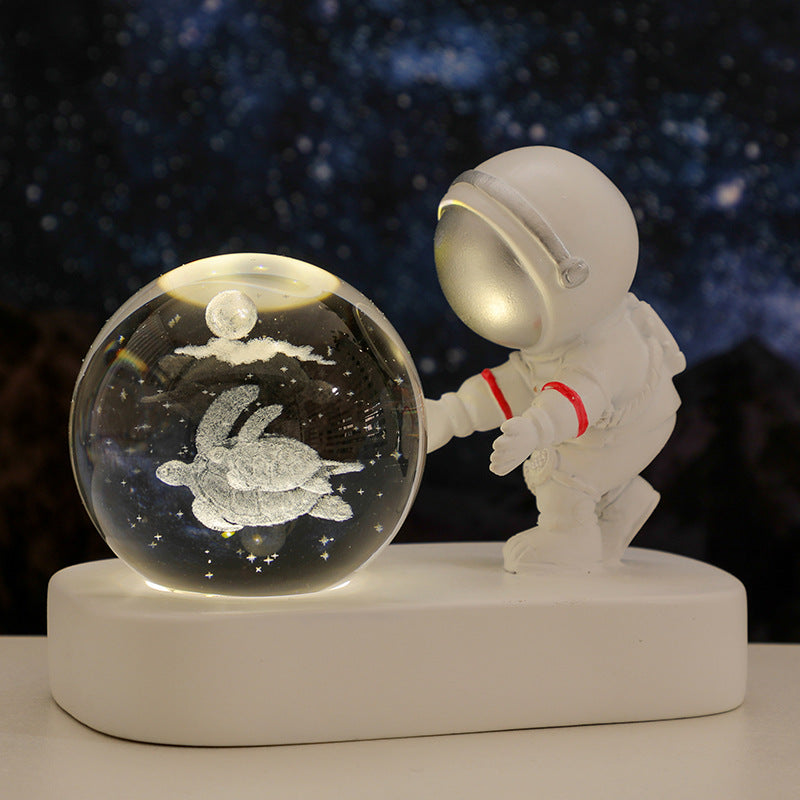 White astronaut figurine touching a glowing glass orb with a turtle and moon inside against a starry night background