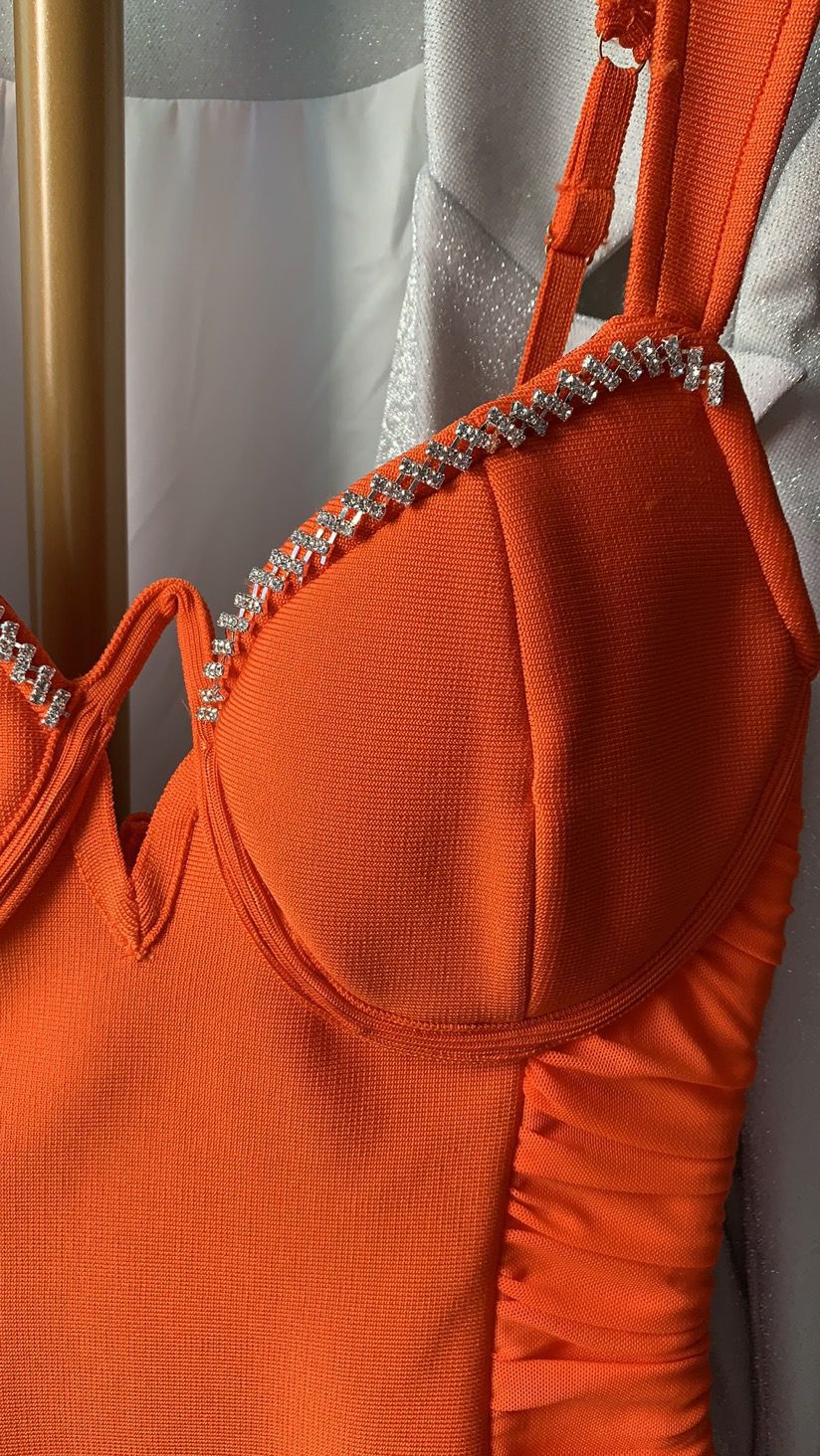 Close-up of orange dress with rhinestone strap embellishments hanging near white garment