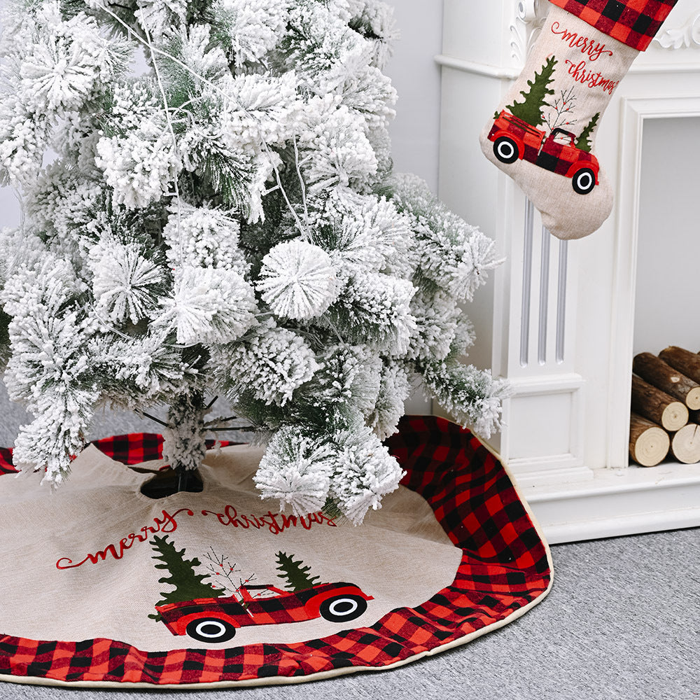 Snow-frosted Christmas tree with red plaid and beige tree skirt and matching Merry Christmas stocking by white fireplace