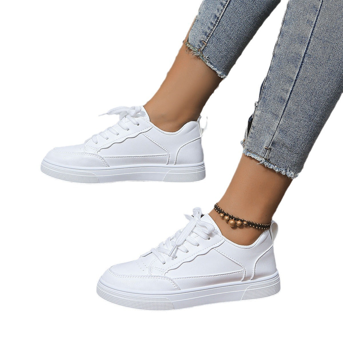 White casual lace-up sneakers on feet wearing cropped blue jeans and a beaded ankle bracelet