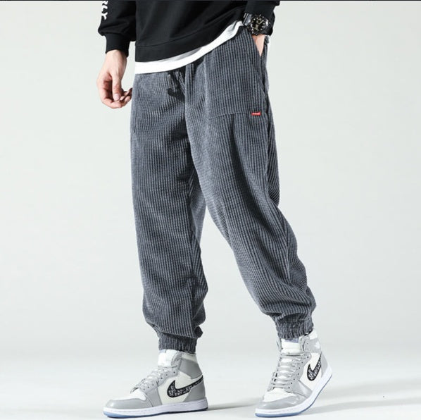 Male model wearing gray ribbed jogger pants and white-gray Nike high-top sneakers on light background