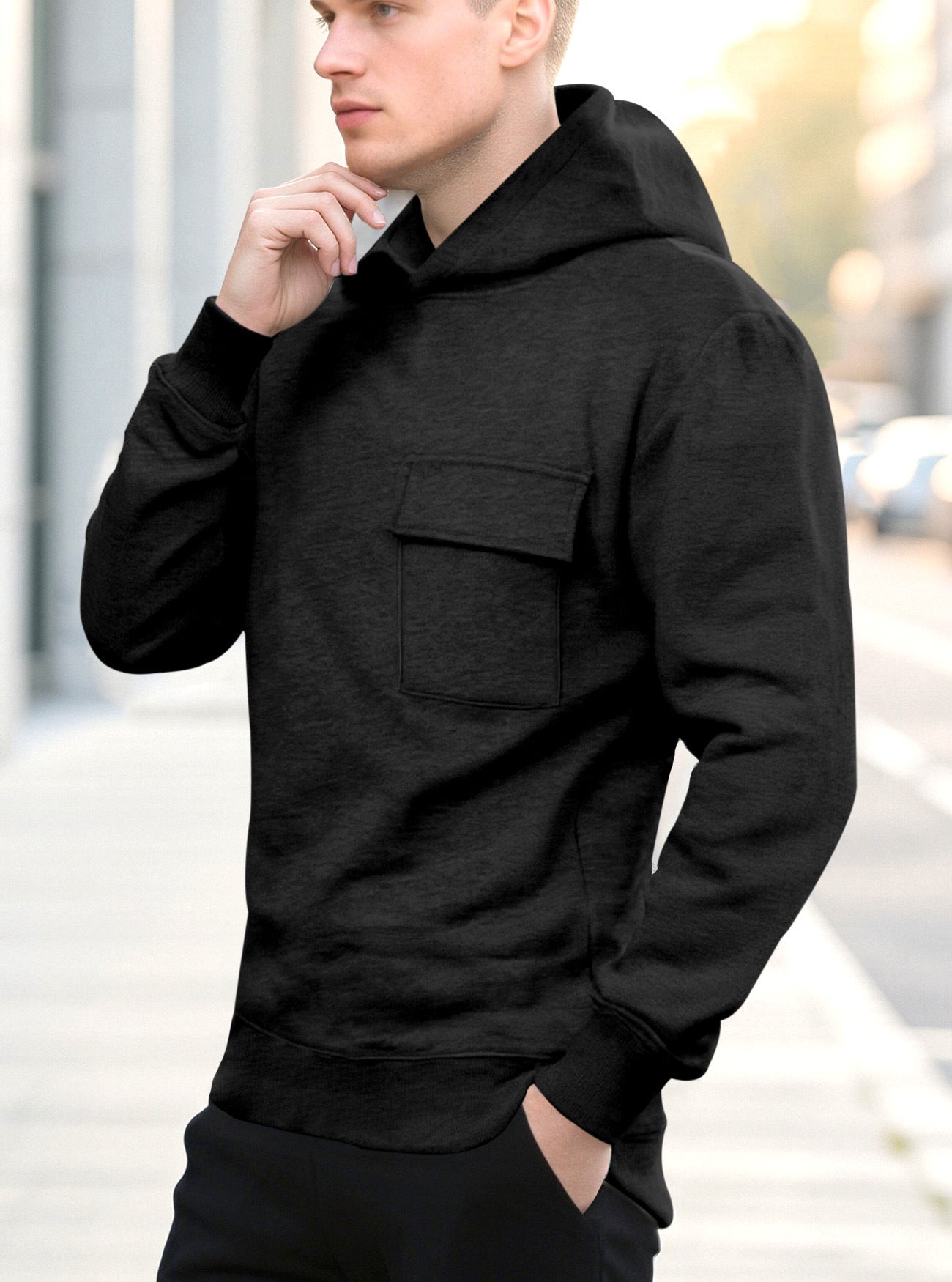 Young man wearing a black hoodie with front pocket standing on a city sidewalk