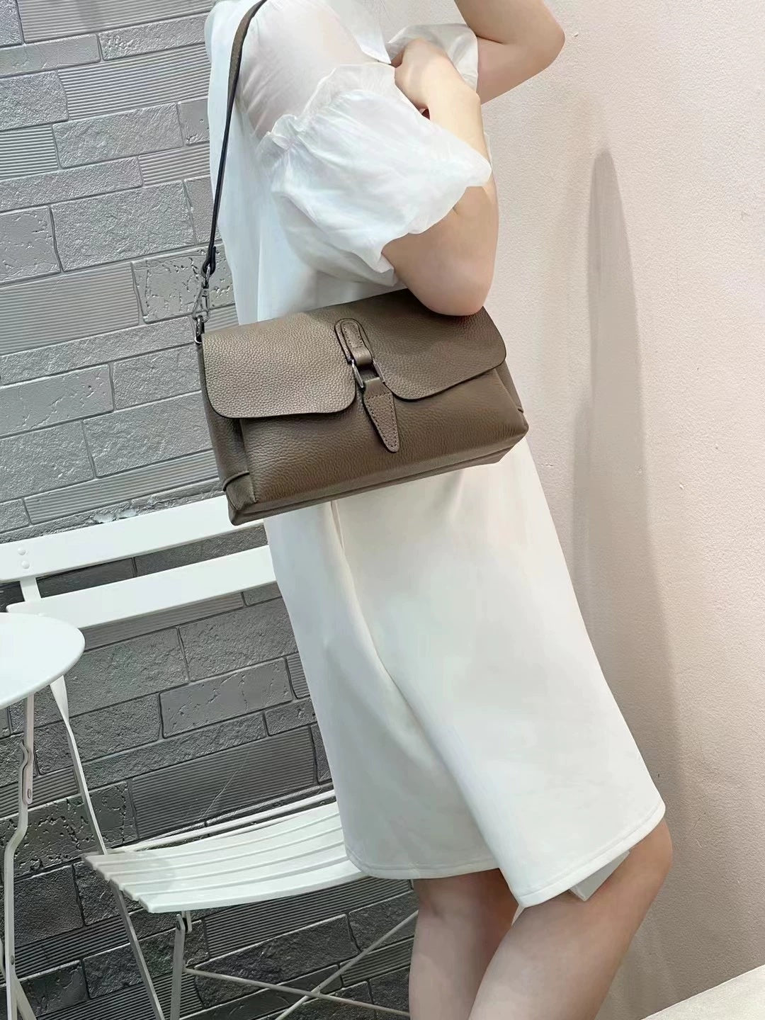 Woman in white dress holding brown leather crossbody bag with buckle detail