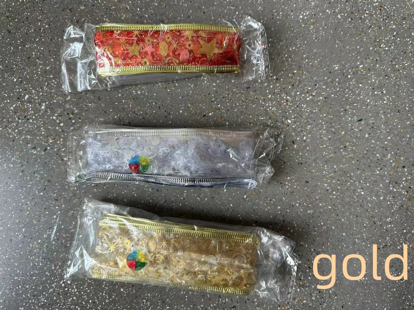 Three decorative ribbon trims in red, silver, and gold packaging on a speckled gray surface