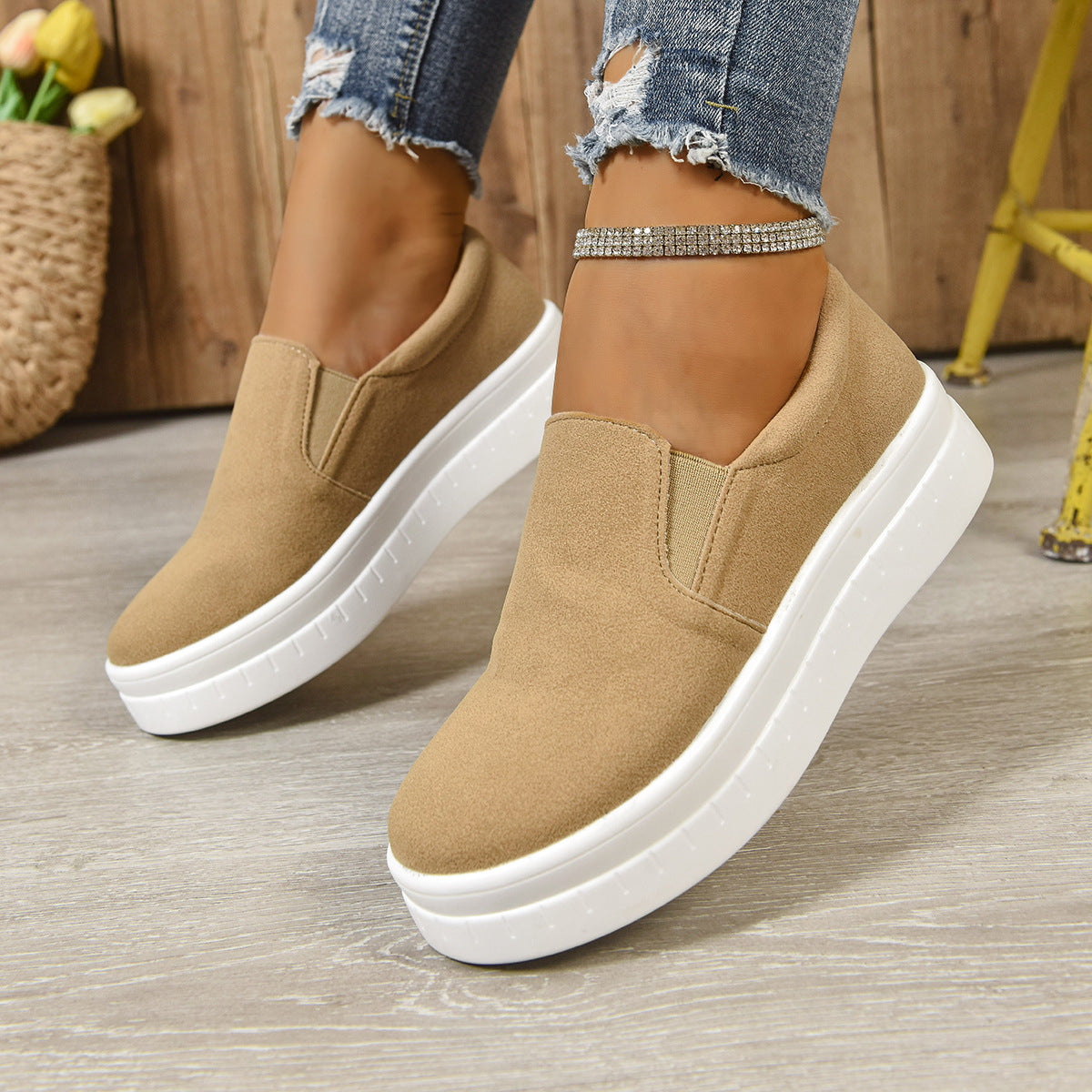 Close-up of beige slip-on platform sneakers with white soles worn with ripped blue jeans and rhinestone anklet