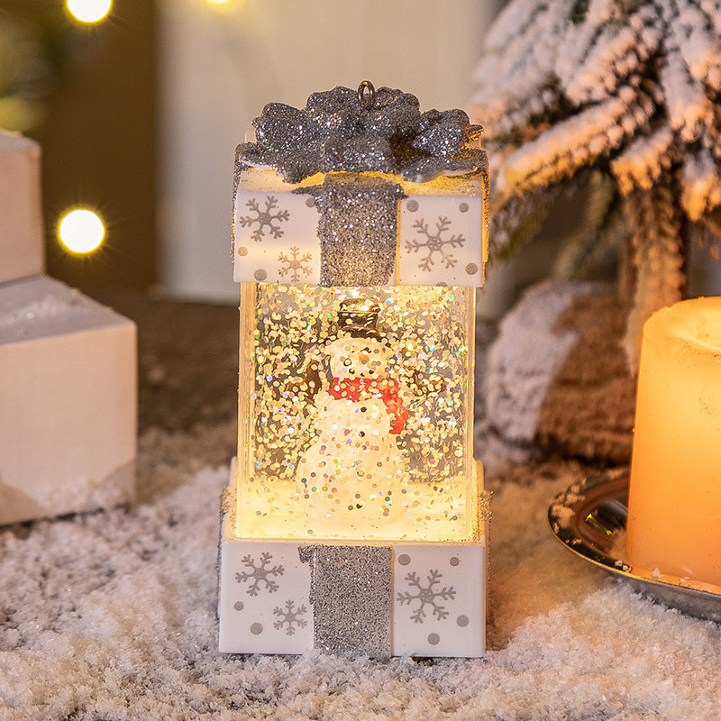 Glittery snow globe gift box ornament with snowman inside, illuminated, on snowy surface near candle