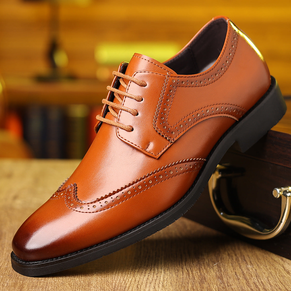 Tan brown leather men's dress shoe with brogue detailing and black sole on wooden surface