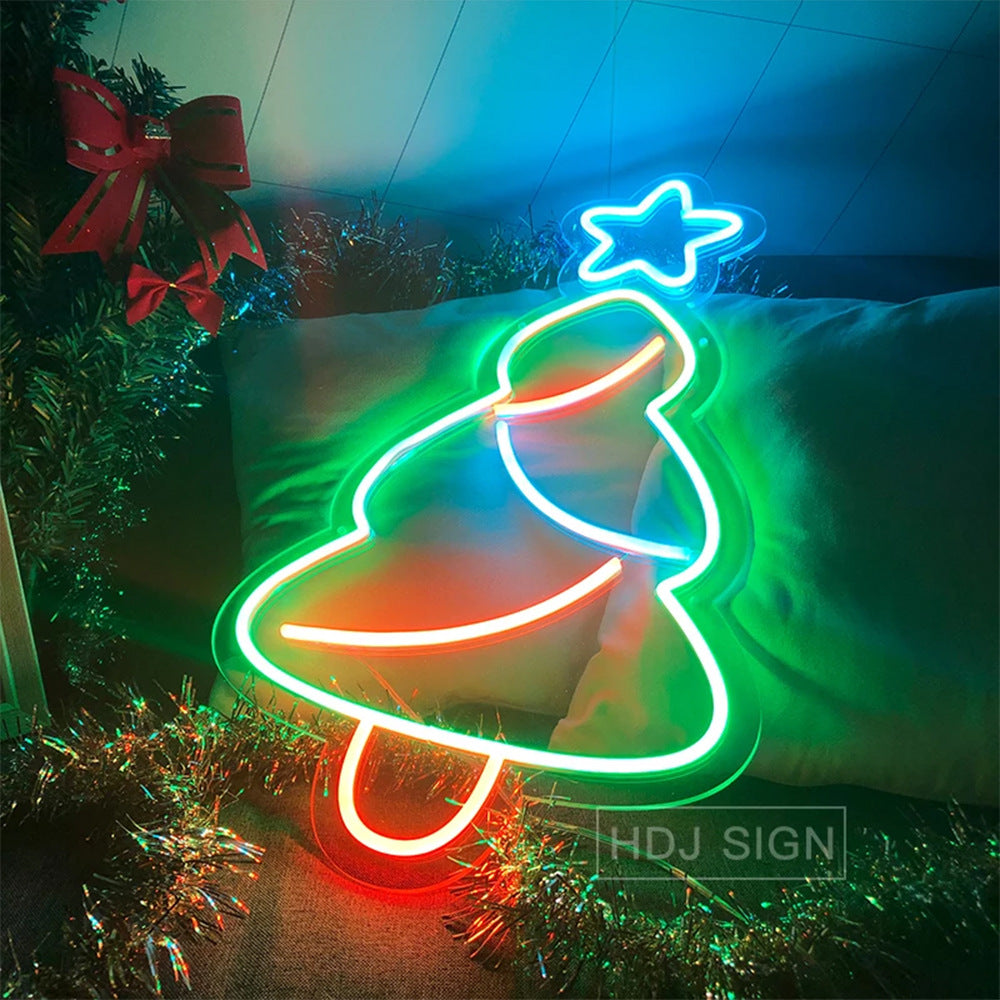 Neon Christmas tree sign with green outline, red base, and blue star on pillow, festive decor