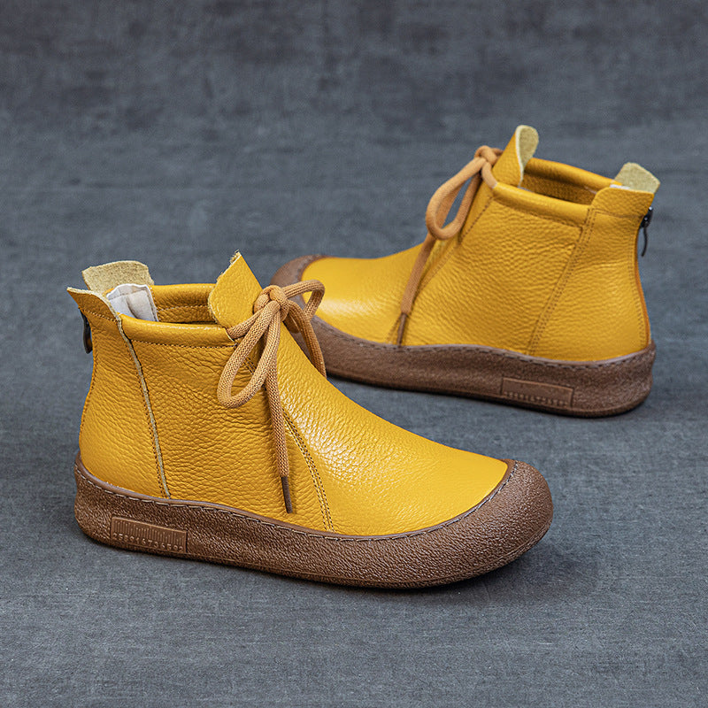 Yellow leather ankle boots with brown rubber soles and laces on gray surface