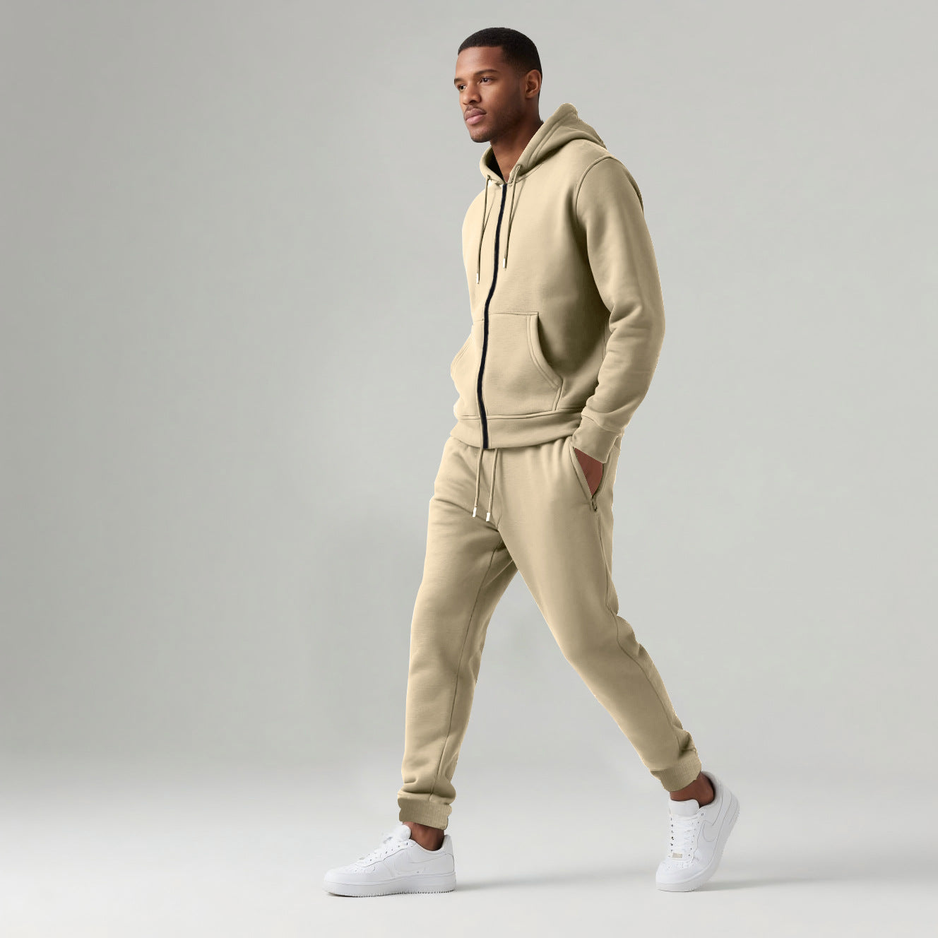 Man wearing beige hooded cotton blend tracksuit and white sneakers on gray background