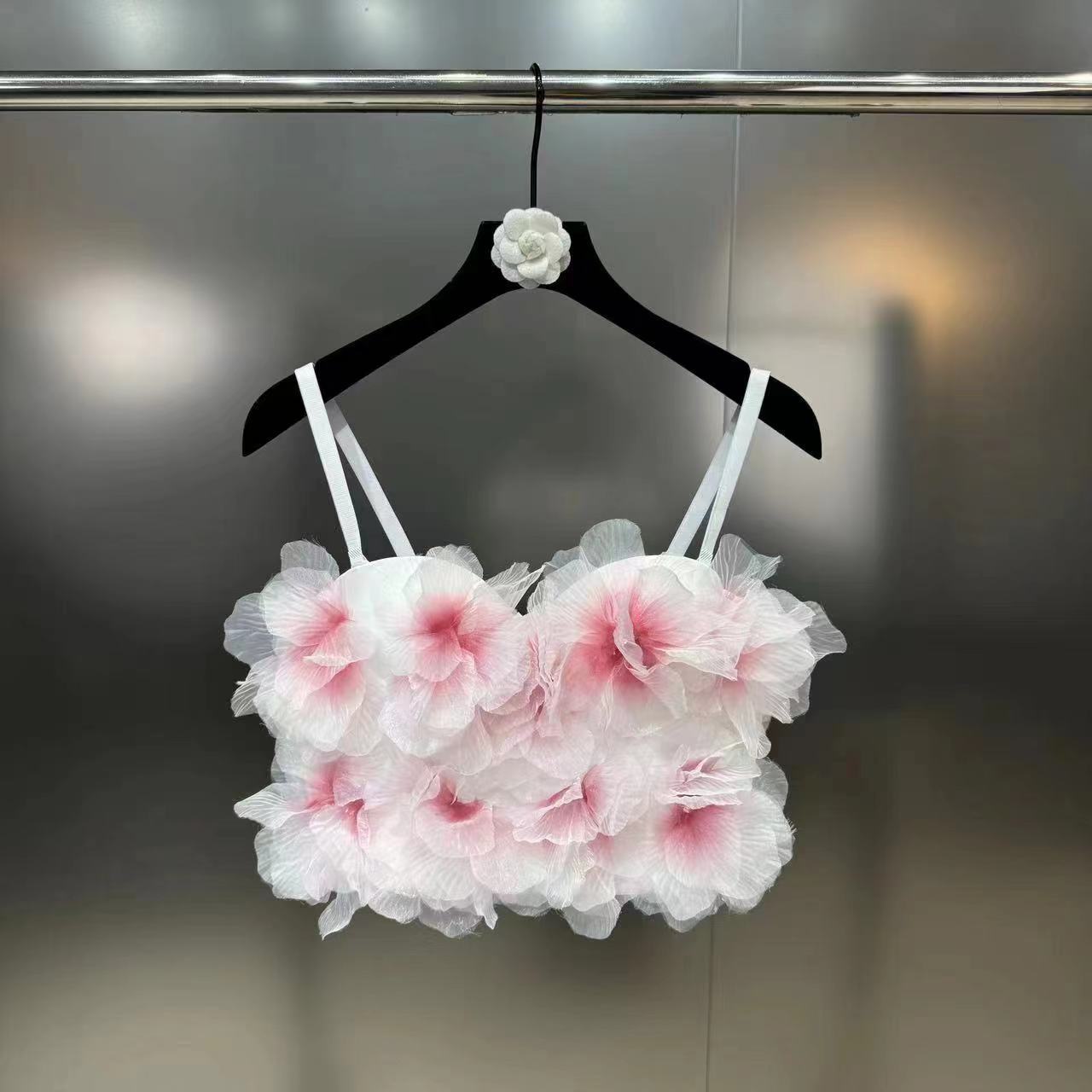 White crop top with pink flower petal accents hanging on black velvet hanger against metallic background