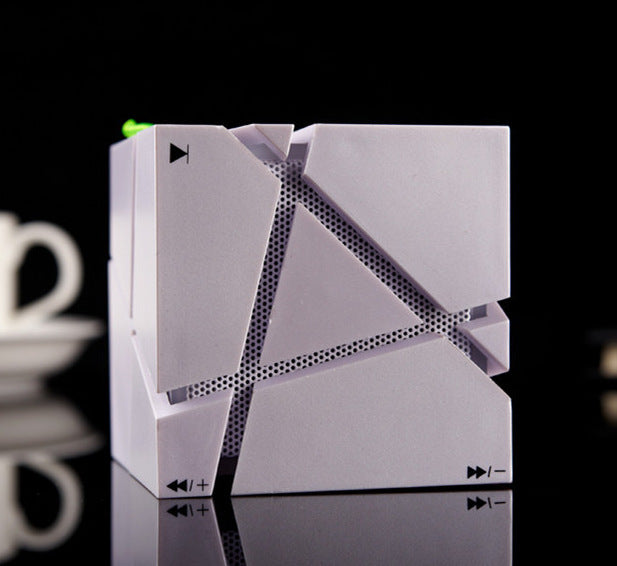 White cube Bluetooth speaker with geometric cutouts and play/pause buttons on a reflective surface