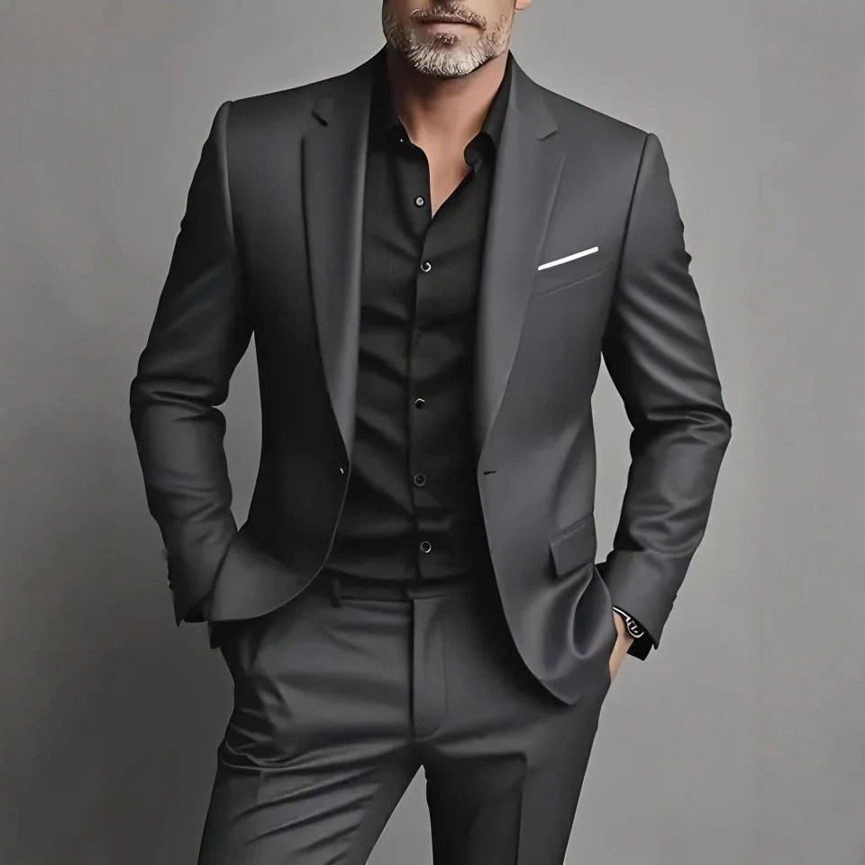 Man wearing black slim fit suit with black shirt and white pocket square on gray background