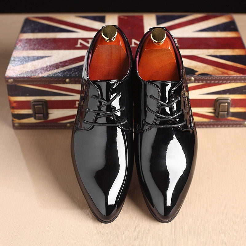 Pair of glossy black patent leather dress shoes with laces on a wooden surface, Union Jack box background