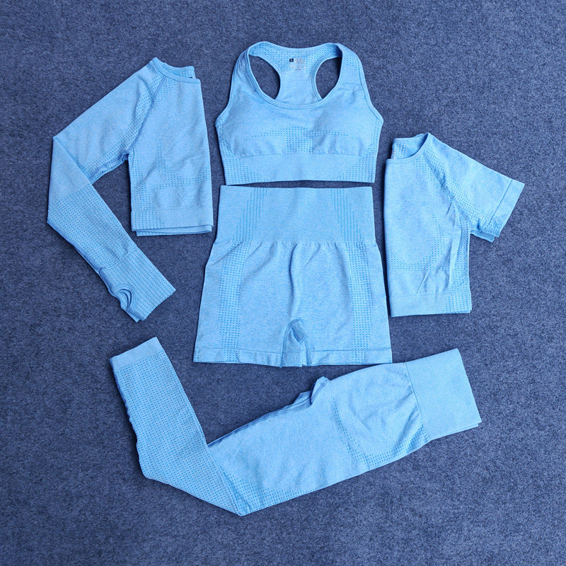 Light blue seamless five-piece activewear set including long sleeve crop top, sports bra, shorts, short sleeve top, and leggings on gray background
