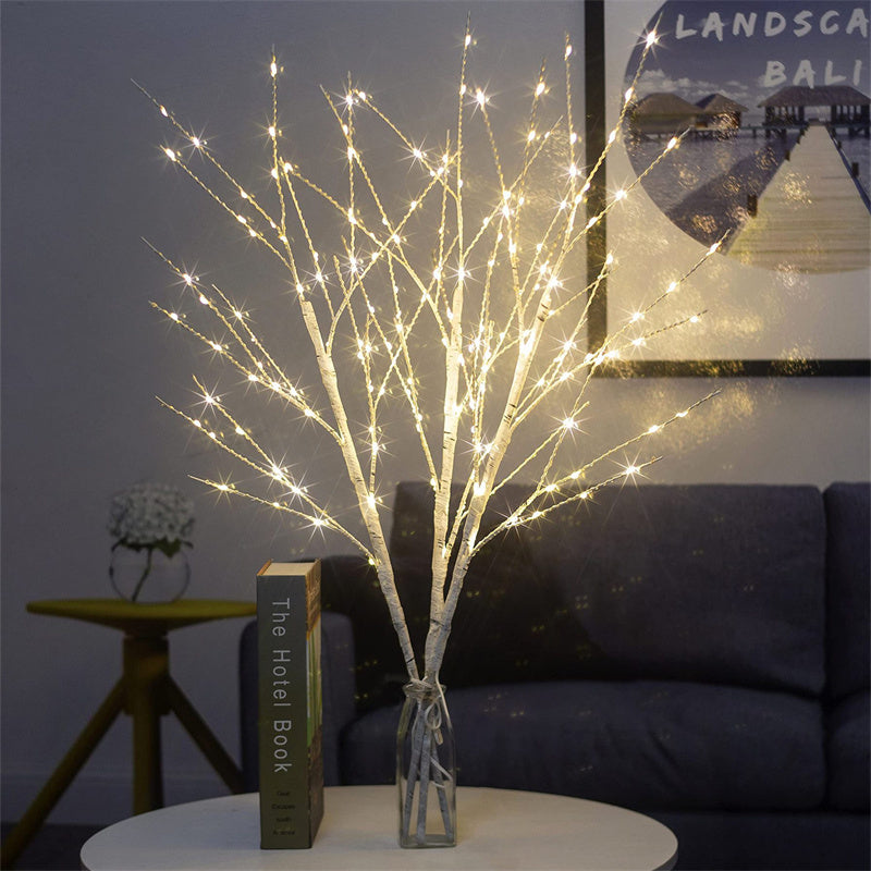 Decorative white birch tree branches with warm white LED lights in glass vase on table in cozy living room