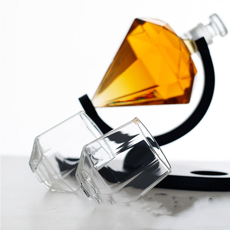 Diamond-shaped whiskey decanter with amber liquid on black stand and two clear whiskey glasses