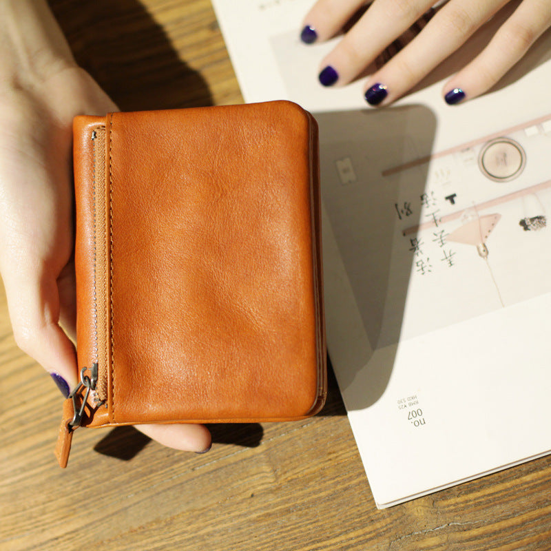 Hand holding slim brown leather bifold wallet with zipper on wooden table beside book with Asian text