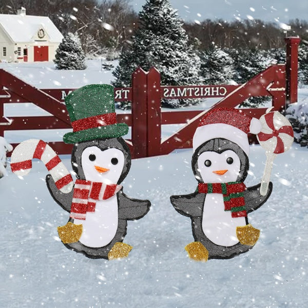 Two glittery penguin Christmas lights in snow, one with green top hat the other with Santa hat, holding candy cane and peppermint