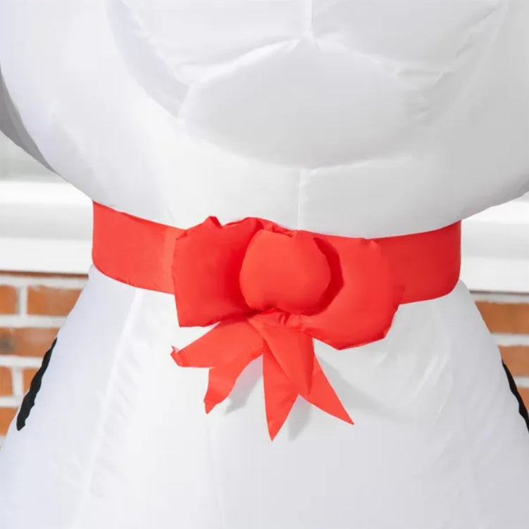 Close-up of white inflatable holiday decoration with large red bow on brick background