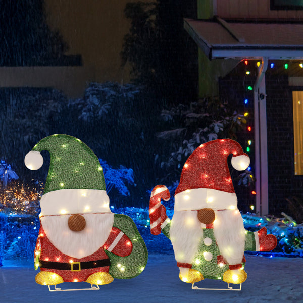Outdoor Christmas decorations featuring two lighted gnomes with candy canes in snow at night