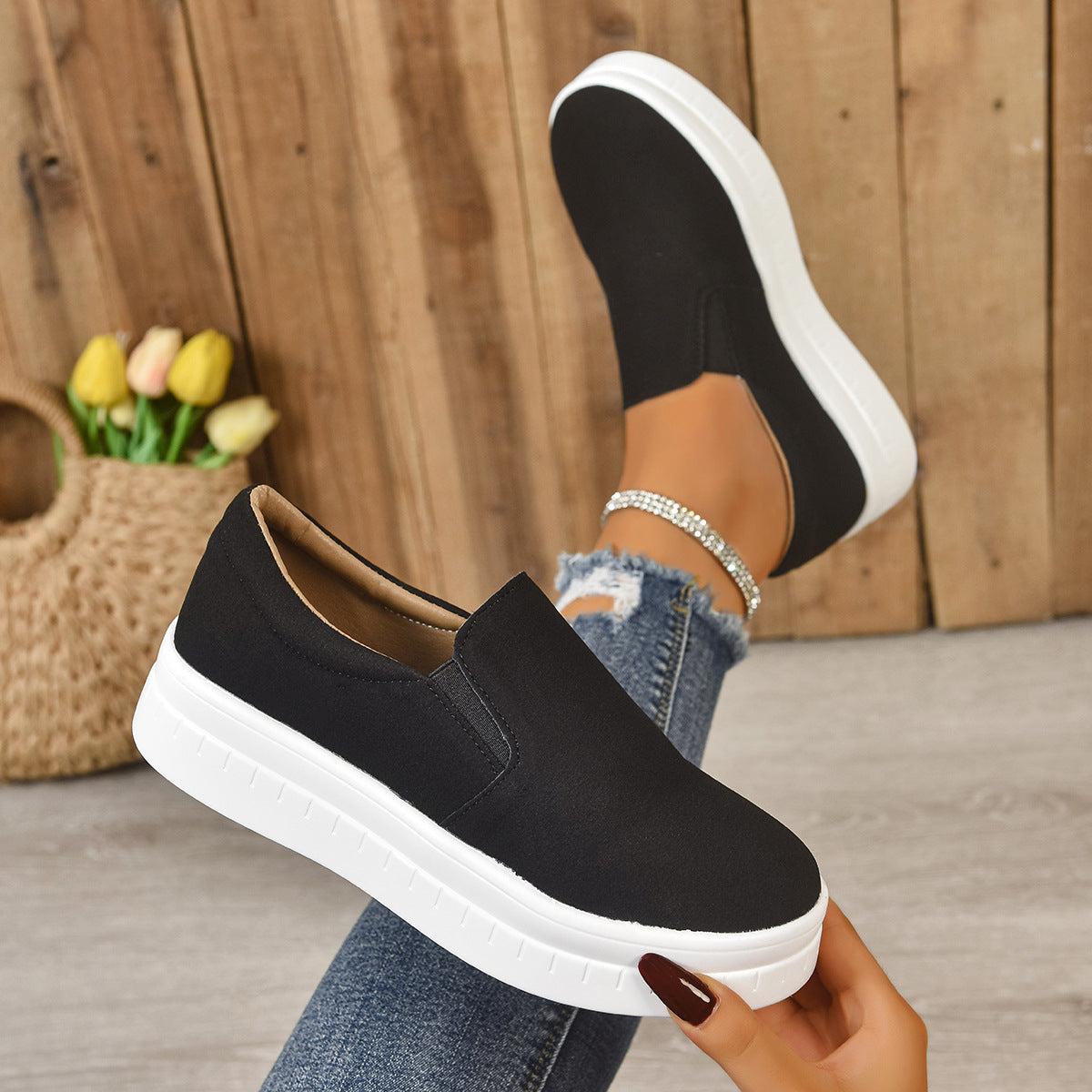 Black slip-on platform sneakers with white soles worn with ripped blue jeans and rhinestone anklet
