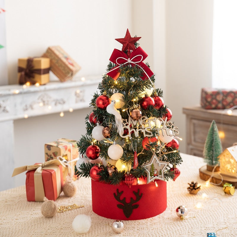 Small decorated Christmas tree with red and white ornaments, lights, and red star topper on table