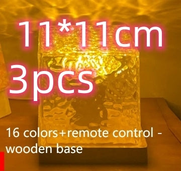 Decorative glass cube lamp with wooden base glowing warm yellow on wooden surface