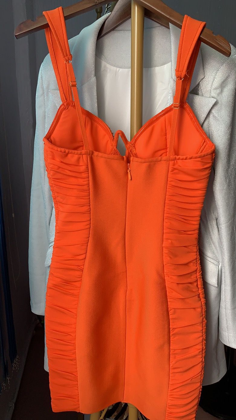 Orange ruched bodycon mini dress with adjustable straps hanging on wooden hanger with white blazer