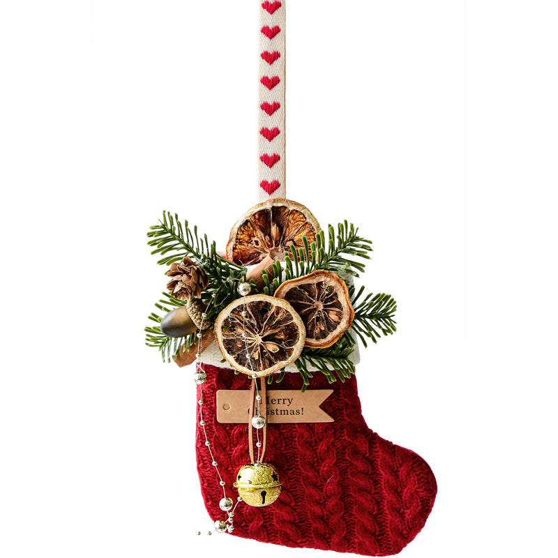 Red knitted Christmas stocking with dried orange slices, pine sprigs, pinecone, and gold jingle bell ornament