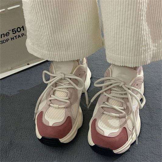 Close-up of white and pink mesh chunky sneakers with thick soles and laces, worn with cream corduroy pants