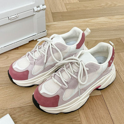Pair of white and pink mesh athletic sneakers with chunky sole on wooden floor