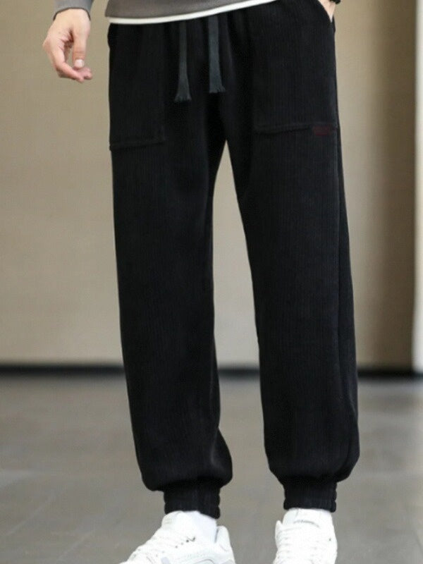 Black ribbed jogger pants with drawstring and cuffed ankles worn with white sneakers