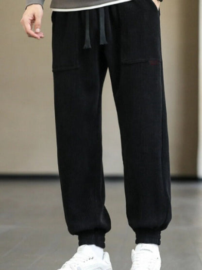 Black ribbed jogger pants with drawstring and cuffed ankles worn with white sneakers