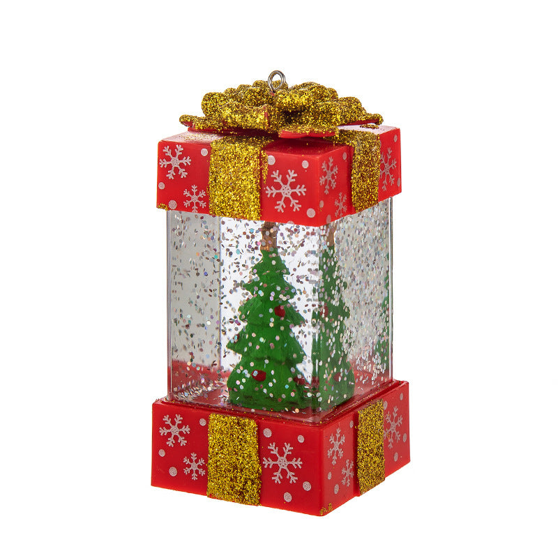 Christmas ornament shaped like a red gift box with gold glitter bow and snowflakes, containing green trees inside