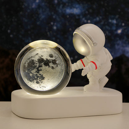 White astronaut figurine holding illuminated glass moon globe on white base against starry background