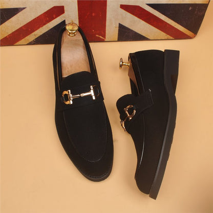Black suede men's loafers with gold horsebit buckles on tan background and Union Jack flag