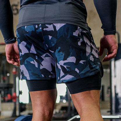 Close-up of a man wearing black and blue camo workout shorts with compression leggings in a gym setting