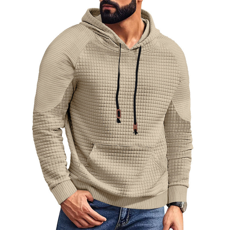 Bearded man wearing beige textured quilted hoodie with black drawstrings and blue jeans
