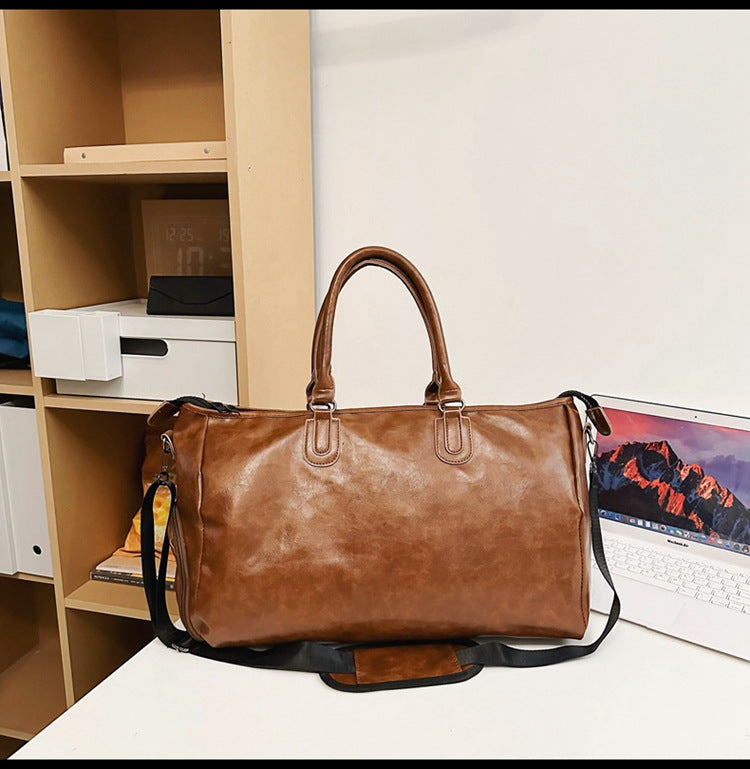 brown leather duffel bag on white table with wooden shelf and laptop in background