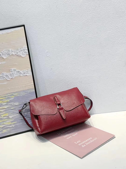 Red leather handbag with buckle detail on white table against gray wall, next to framed sea painting