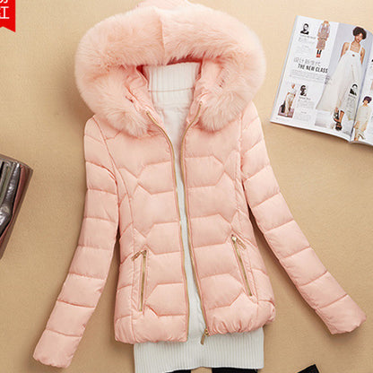 Soft pink women's puffer jacket with faux fur hood and gold zipper details on beige surface