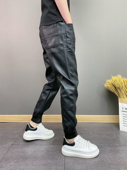 Person wearing black faux leather jogger pants with back pockets and white platform sneakers on gray tile floor
