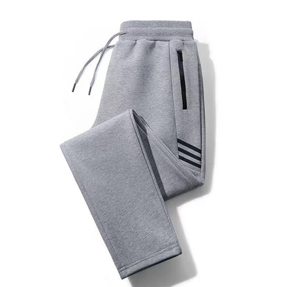Folded grey sweatpants with drawstring waist and black zippered pocket, featuring three black stripes near ankle