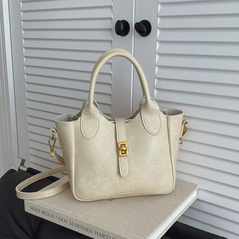 Cream leather handbag with gold clasp on a hardcover book in front of white louvered doors