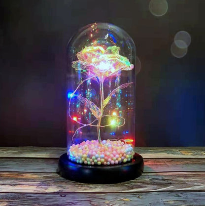 LED lighted glass dome with a multicolored glowing artificial rose on a wooden surface